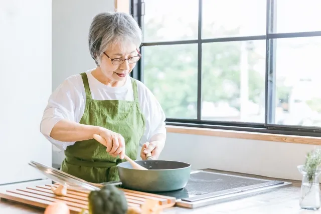 高齢の女性が台所で料理をしている